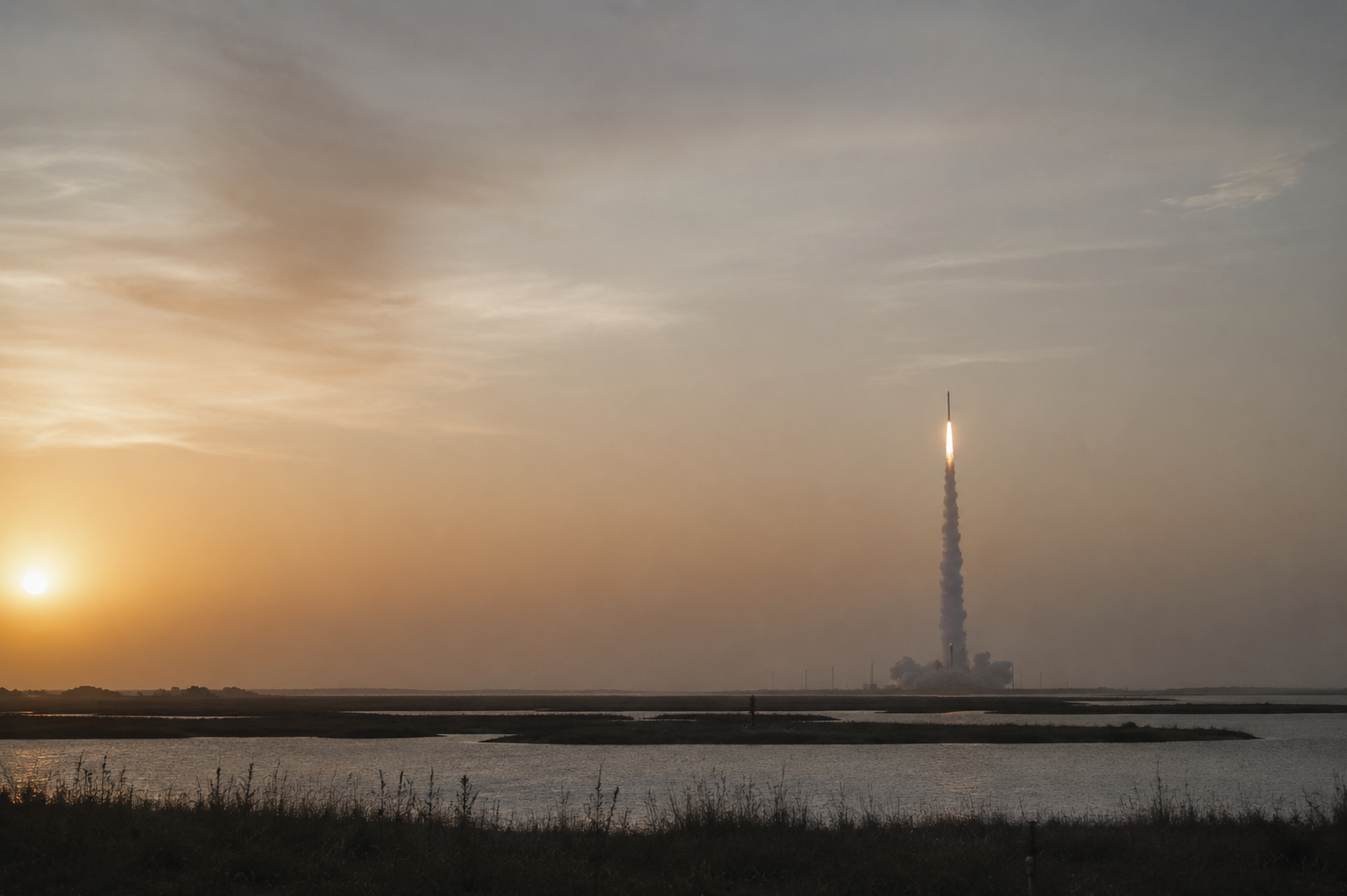 Rocket lifting off over a coastal landscape at dawn