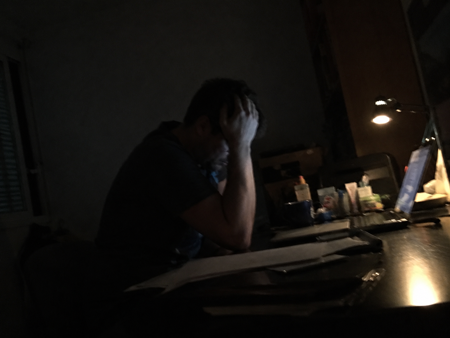 Exhausted person at a cluttered desk late at night